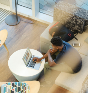 Young man sitting in a lobby browsing his laptop.