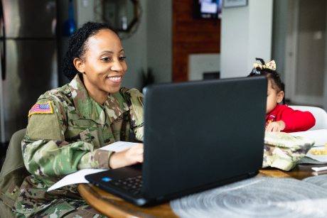 Young woman sitting at a table with her baby girl and looking at her laptop.  